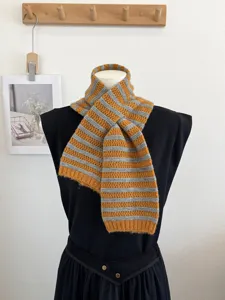 Detailaufnahme des kuscheligen gelb-grau gestreiften Strickschals mit Kreuz-Wickeldesign.