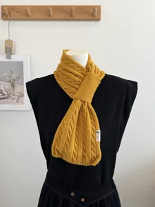 Detailed view of the yellow cable knit cross scarf showcasing soft woolen texture and small label.