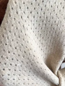 Beige knitted hollow fabric detail close-up showing soft texture and delicate pattern.