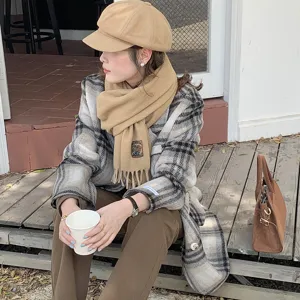 Detail view of cozy solid color scarf with fringe, lifestyle shot with plaid coat outfit.