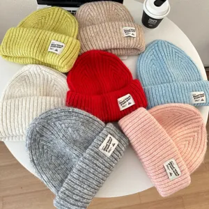 Detail view of colorful woolen knitted winter beanies with woven label, cozy warm headwear