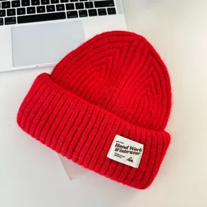 Red wool blend knit beanie detail, warm winter cuffed hat with woven patch and soft texture.