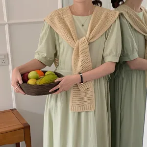 Close-up detail of the beige hollow-out knitted shawl tied over a sweet light green dress.