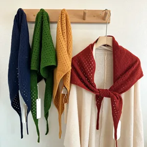 Detailed view of hollow knitted wool triangular scarves hanging on wooden hook, soft knitwear style.