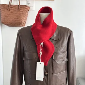 Dettaglio della sciarpa incrociata in lana lavorata a maglia rossa, texture morbida invernale.