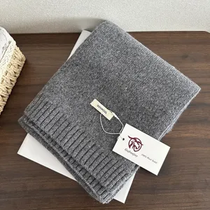 Detailed close-up shot of a soft grey knitted wool scarf folded neatly on a wooden table.