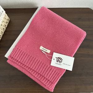 Detail view of a soft pink wool knit scarf with brand tag, perfect for winter warmth.