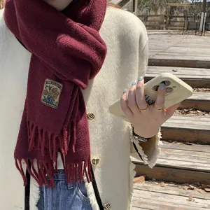 Closeup detail of a cozy maroon winter knitted scarf with fringe and stylish woven label.