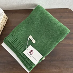 Green wool knit scarf texture detail, folded neatly on wooden table with brand tag.
