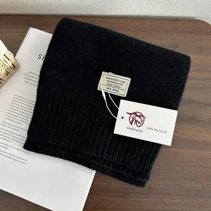 Close-up detail of a soft black wool knitted scarf folded neatly on a wooden surface.