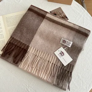 Close-up detail of cozy brown plaid wool scarf with soft tassels and branded tag on white table