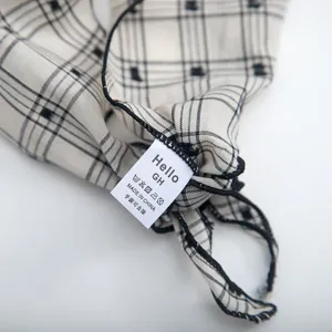 Close-up detail of the black and white plaid triangle scarf, showing embroidery and tag.