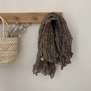 Detailed view of a vintage wrinkled floral scarf hanging on wooden hook with flowers.