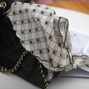 Detailed close-up view of black and white plaid embroidered neck scarf draped on a chic bag.