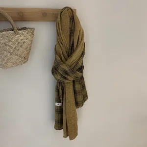 Vue détaillée du foulard à carreaux en lin et coton léger suspendu à un crochet en bois.