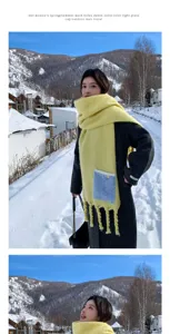 Dicker warmer gelber Winterschal mit blauer Tasche und Fransen in verschneiter Berglandschaft.