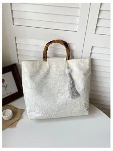 Nahaufnahme Detail der weißen Stofftasche mit elegantem Bambusgriff und grauen Quastenakzenten.