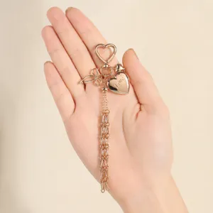 Rose gold heart keychain detail, bow accent and chain tassel charm showing fine metal texture.