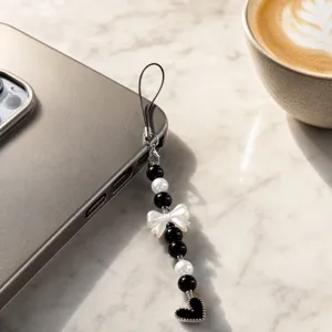 Detailed shot of a chic black and white pearl phone charm featuring a delicate bow and heart pendant.