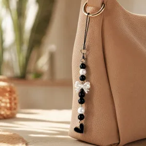 Chic black and white pearl phone charm with cute bow and heart pendant for daily use.