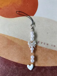 Close-up detail of Korean style pearl bow phone strap charm with white heart pendant.