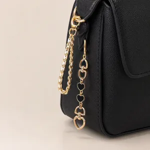 Black leather bag detail showing chic gold chain strap and cute black heart enamel charms.