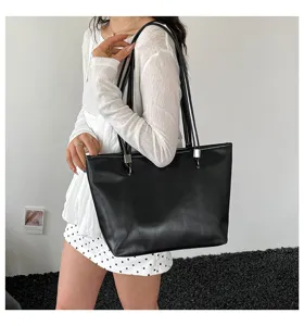 Dettaglio borsa shopper nera minimalista con spallacci sottili e accessori metallici.