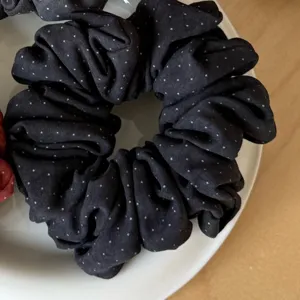 Close-up detail of dark brushed fabric scrunchie with tiny white dots resting on white plate.