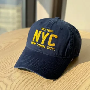 Detailed close-up of a navy blue baseball cap with yellow NYC embroidery and curved brim.