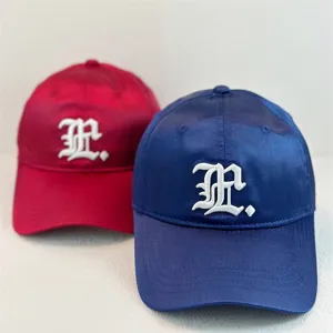 Satin baseball cap detail featuring white gothic embroidery on red and blue fabric surfaces.