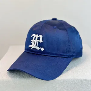Detail shot of dark blue satin baseball cap featuring white gothic letter embroidery design.