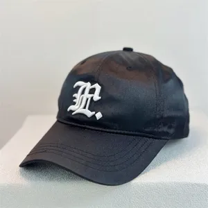 Close-up detail of black satin baseball cap with white embroidered letter for outdoor sun protection.