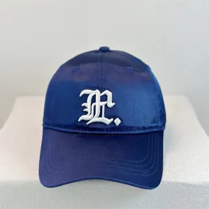 Detail shot of the navy satin baseball cap featuring delicate white gothic embroidery.