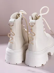 Detail shot of white platform combat boots featuring a unique gold metal snake hanging charm.