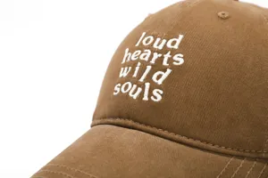 Washed brown cotton baseball cap featuring stylish white embroidered text detail close up.