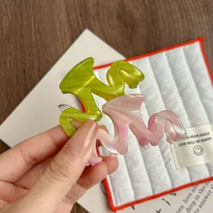 Detailed view of stylish acetate hair claw clip with wavy design in pastel green and pink.