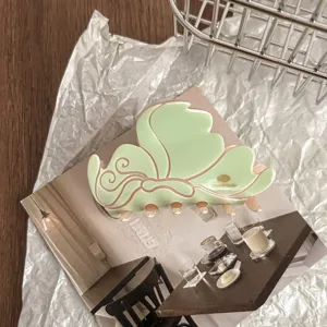 Close-up detail of green butterfly hair claw clip with pink trim, flat lay styling shot.