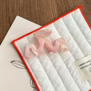 Detailed shot of a stylish pink acetate hair claw clip, featuring a wave design for elegant hairstyles.