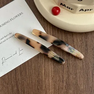 Detail view of tortoiseshell acetate hair clips with elegant gold lettering, perfect for daily styling.