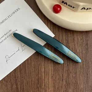 Dark green acetate hair clip detail shot, elegant gold lettering barrette for women styling.