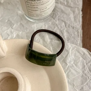 Close-up detail of dark green acetate hair tie with gold handmade lettering and elastic band.