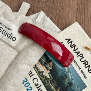 Detailed view of the red curved acetate hair clip, showing glossy finish and minimalist design.