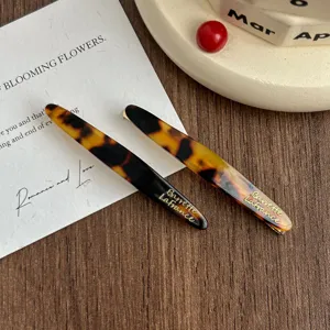 Detailed close-up of tortoise shell acetate hair clips featuring elegant gold lettering.