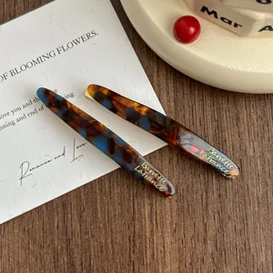Tortoiseshell acetate hair clip detail shot with gold lettering and floral card prop.