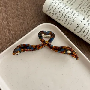 Close-up detail of elegant tortoiseshell hair claw clip displayed on a white ceramic tray.