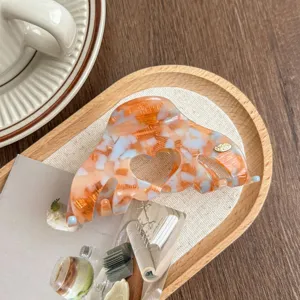Close-up detail of Korean style orange acetate hair claw clip with cute hollow heart design.
