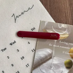 Detail shot of a burgundy minimalist hair barrette featuring elegant gold lettering on wooden desk.