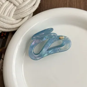 Close-up detail of blue iridescent irregular hair claw clip on white ceramic plate.