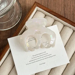 Close-up detail of the elegant white acetate hair claw clip on wooden display tray.