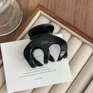 Detailed shot of black acetate hair claw clip, elegant design with golden letter print.